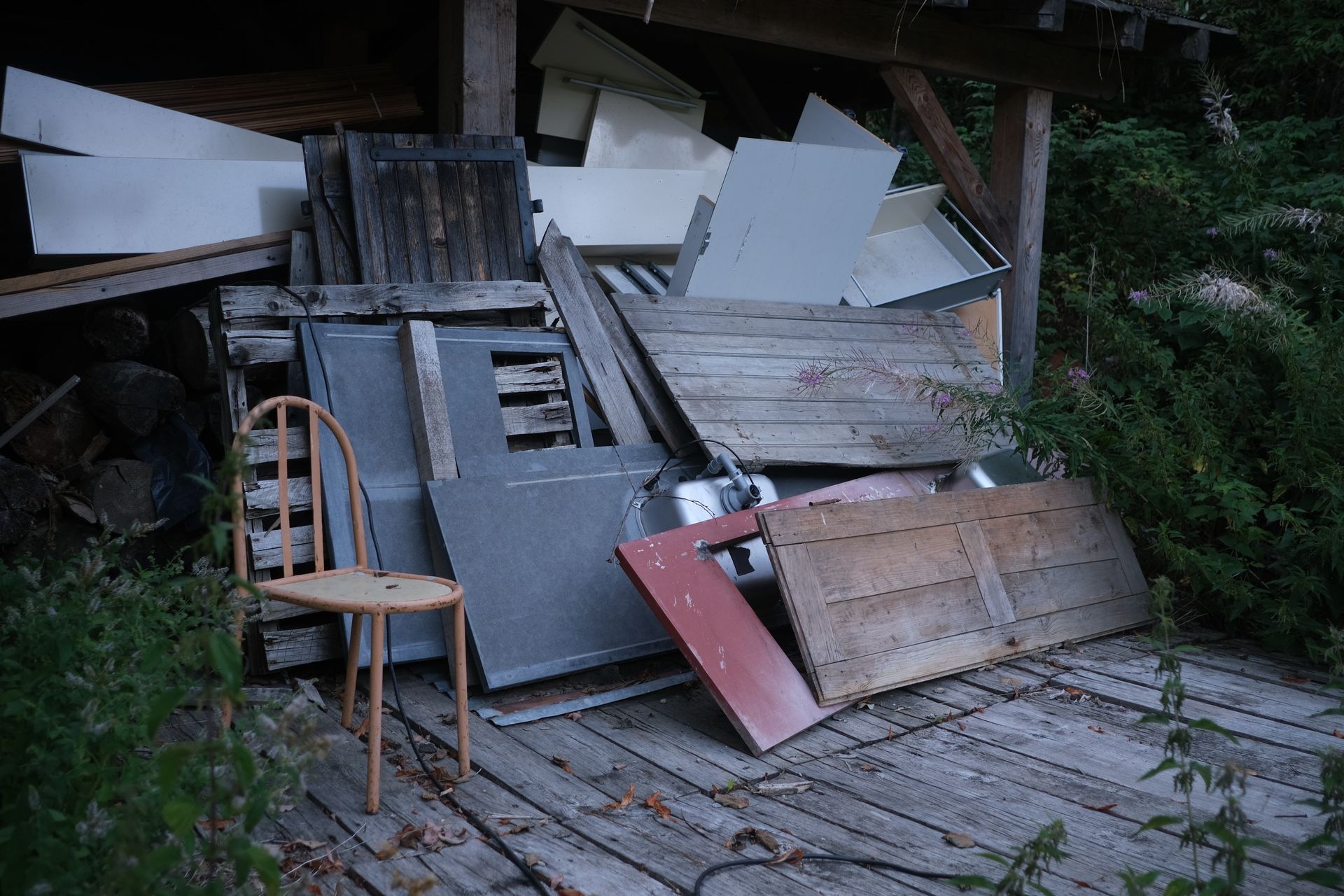 Chaise en bois sur un porche à côté d'un tas de chutes de bois et de portes sous un toit de hangar.