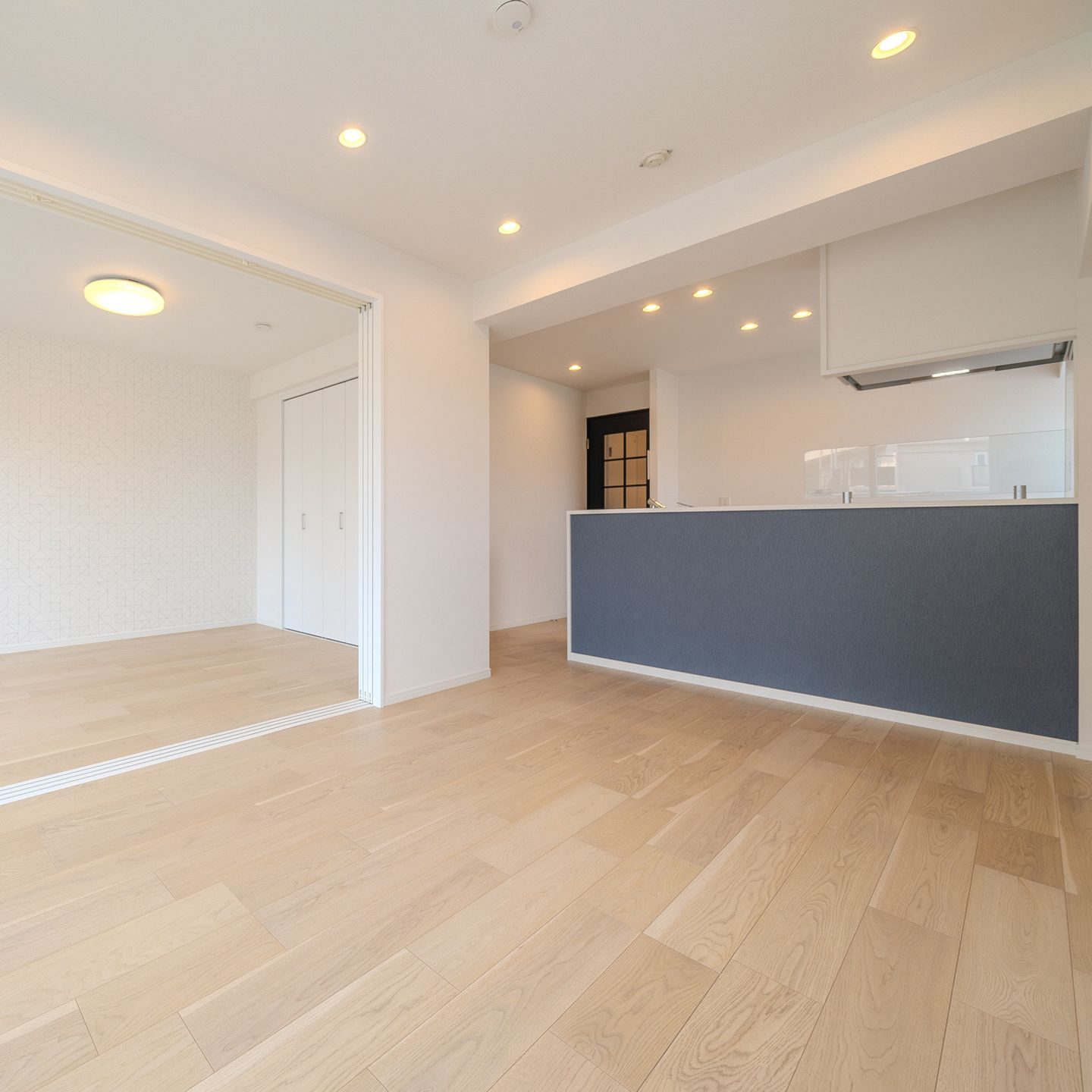 Une pièce intérieure lumineuse et moderne avec parquet clair, murs blancs et îlot de cuisine gris foncé.