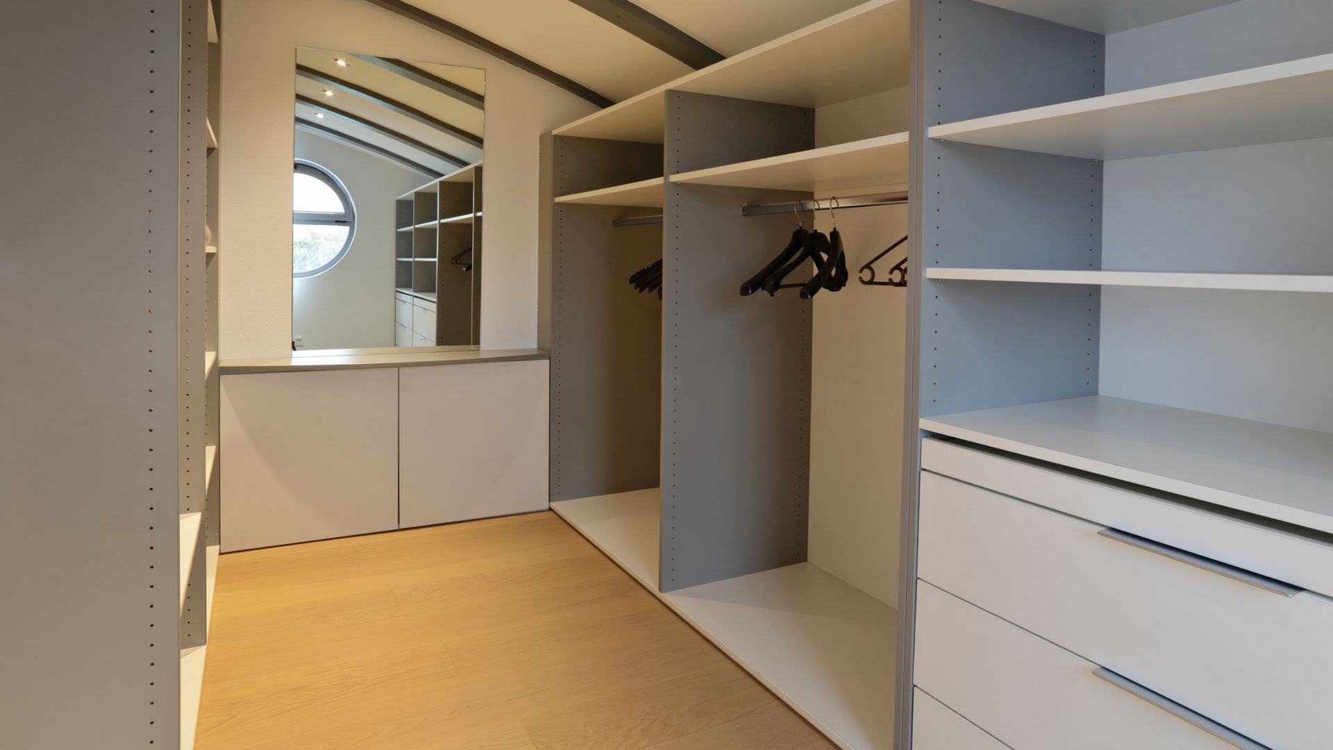 Un dressing avec un sol clair, des placards blancs, des étagères grises, des tringles à vêtements et un mur de miroirs.