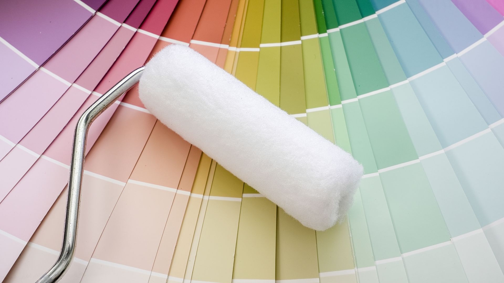 Un rouleau à peinture blanc est posé en diagonale sur un éventail vibrant d'échantillons de peinture colorés.