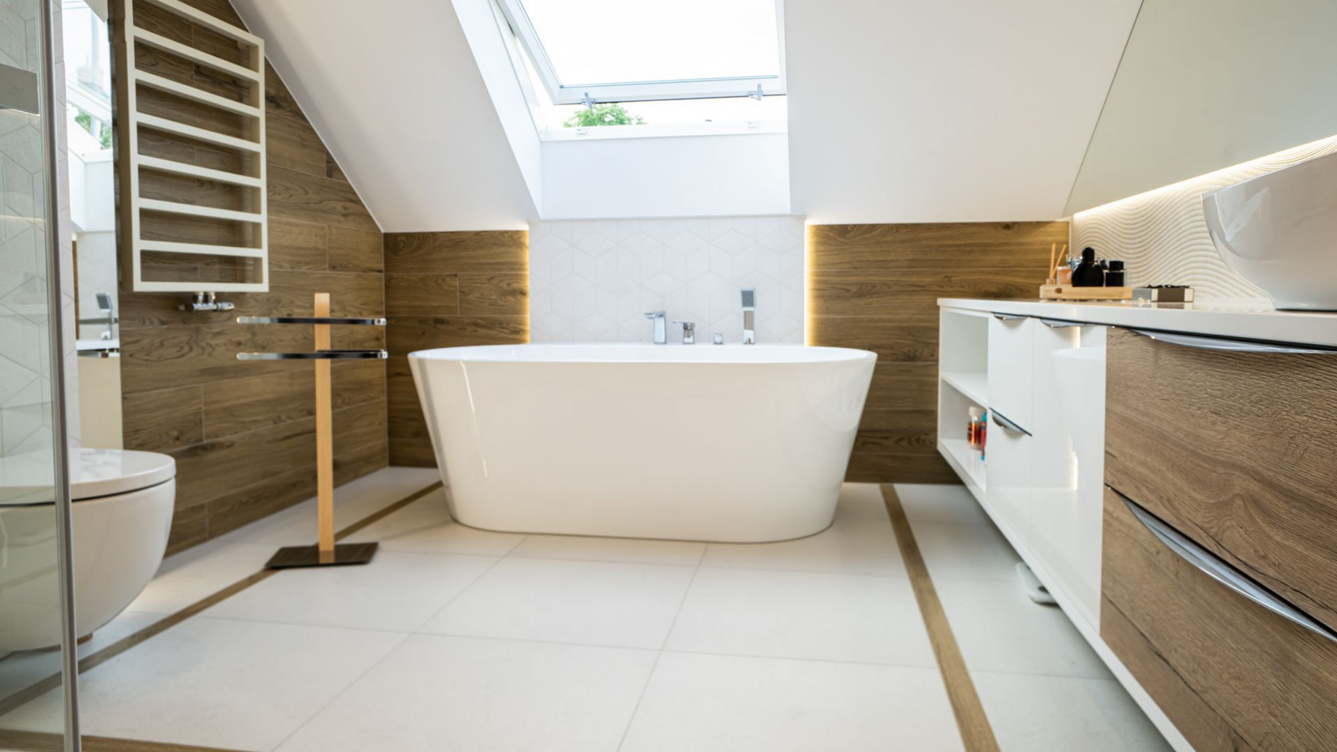 Une salle de bains moderne avec une baignoire blanche sur pieds, des éléments en bois et des armoires blanches sous un plafond mansardé.