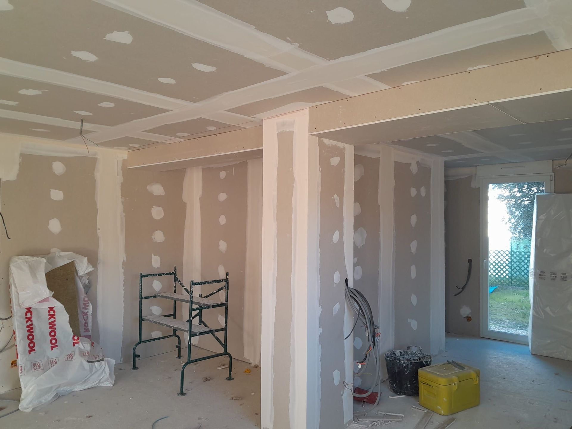 Vue intérieure d'une pièce en construction, montrant les panneaux de plaques de plâtre nouvellement installés sur les murs et les plafonds.