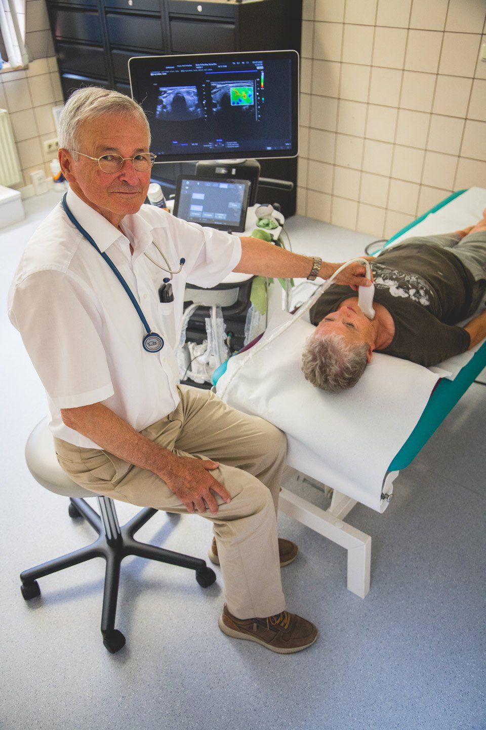 Arzt führt Ultraschall an einem Patienten durch, der auf einem Untersuchungstisch in einer Arztpraxis liegt.