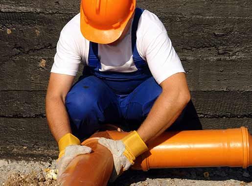 Obrero de la construcción con casco y guantes naranjas manipulando una tubería naranja de gran tamaño.