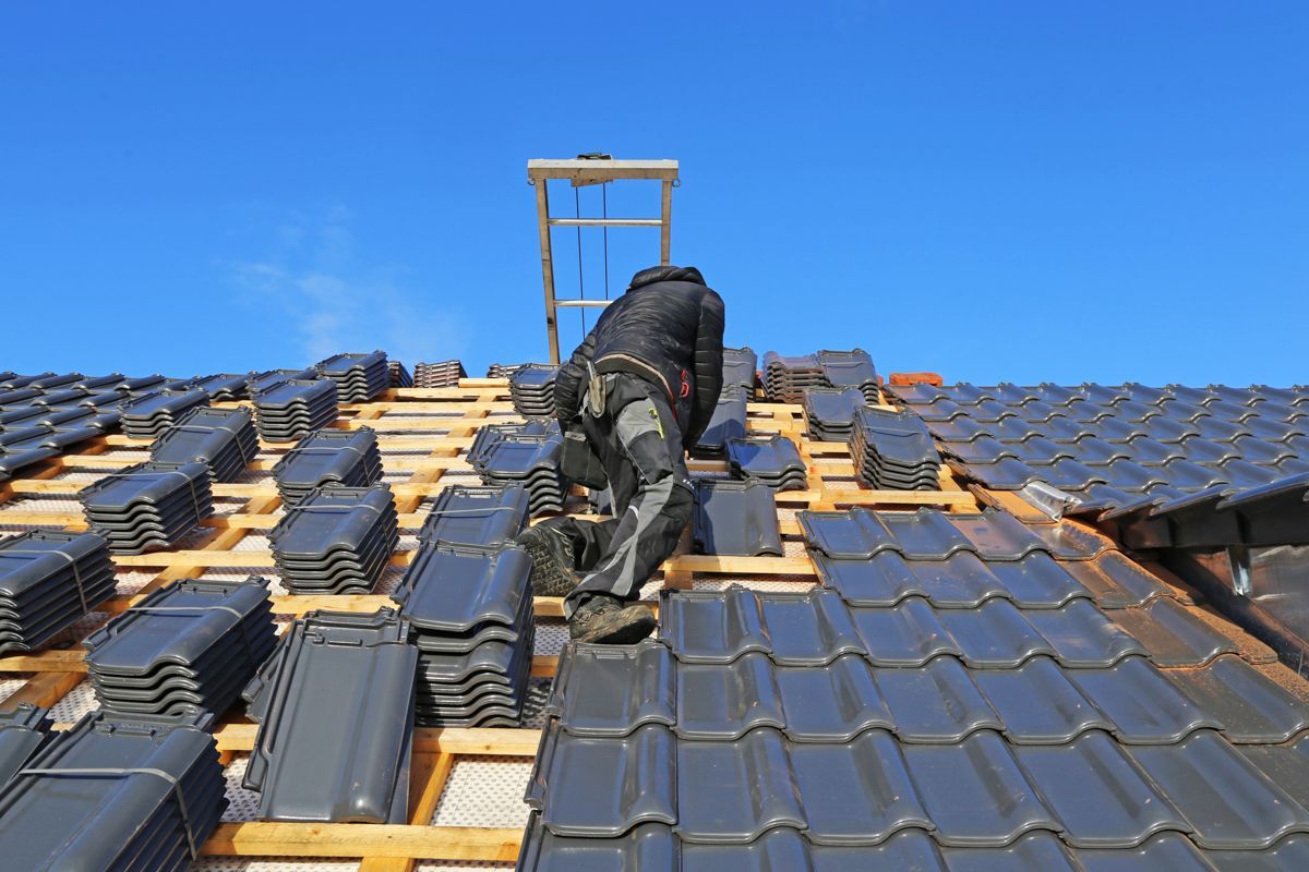 Dachdecker in dunkler Kleidung auf einem Dach vor blauem Himmel.