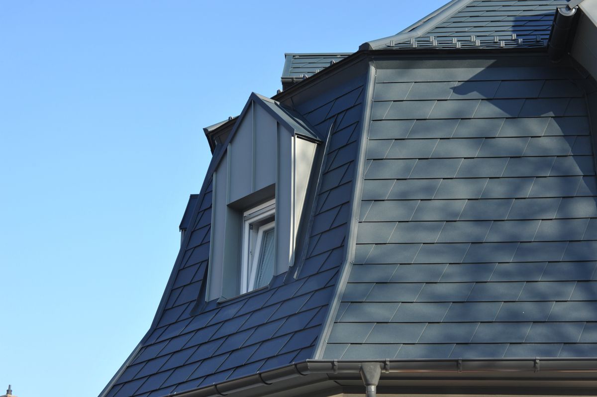Blaues Dach mit Dachgaubenfenster vor strahlend blauem Himmel.