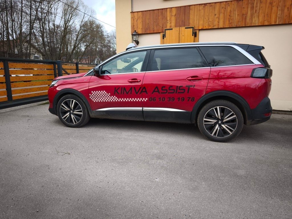 Un homme au volant d'une voiture parle au téléphone ; un avion est visible en arrière-plan.