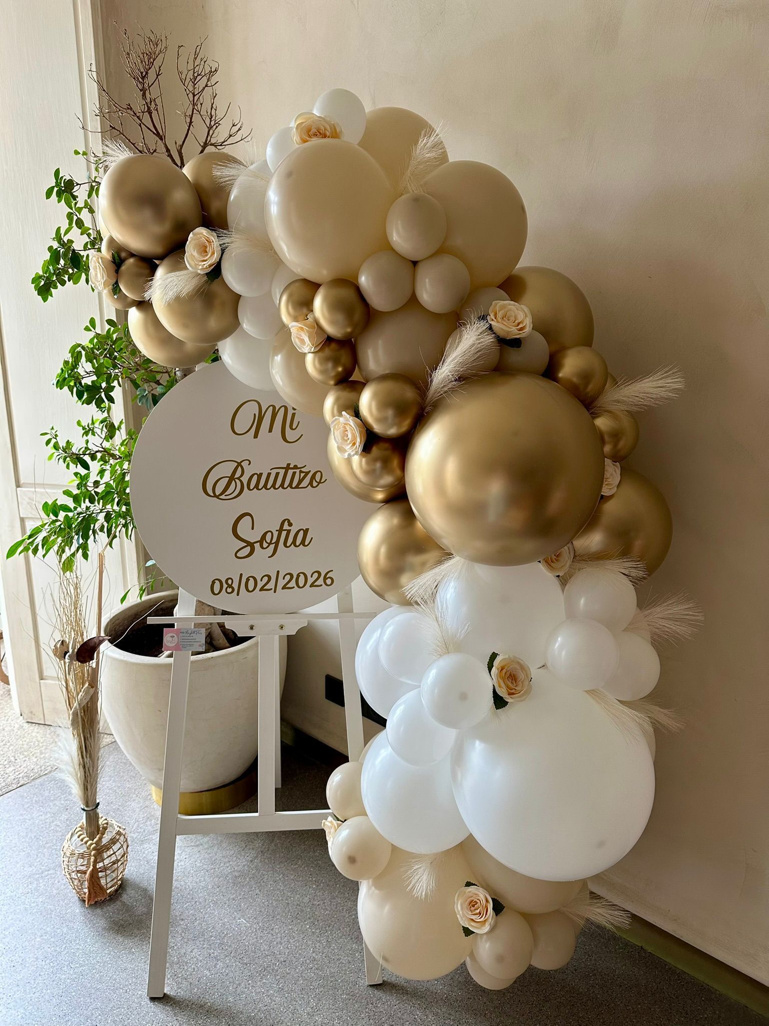 Un cartel con globos y flores está colocado encima de un caballete blanco.