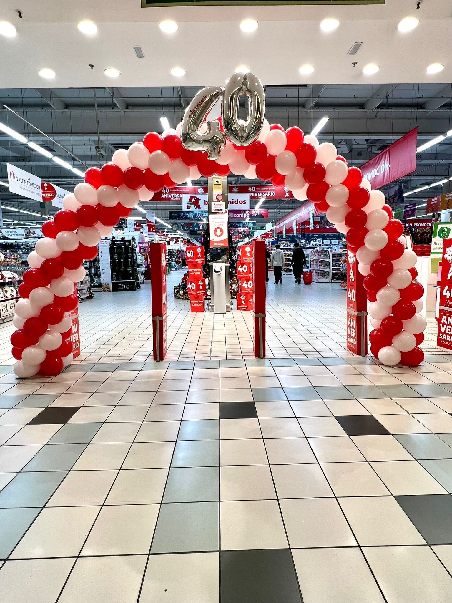 Un arco de globos dorados, plateados y blancos se encuentra frente a un edificio de ladrillos.