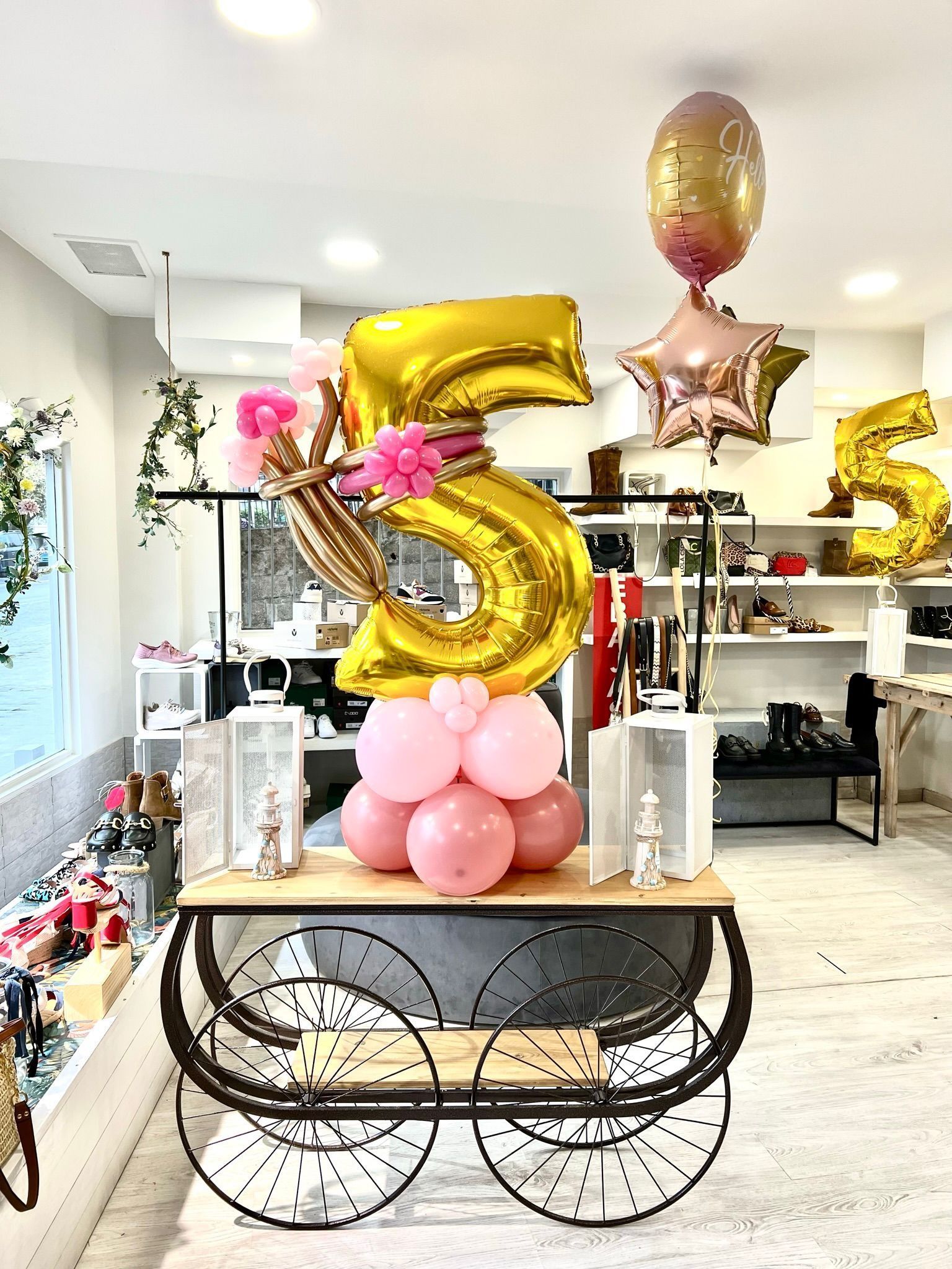 Hay un pastel en un pedestal frente a una pared cubierta de globos.