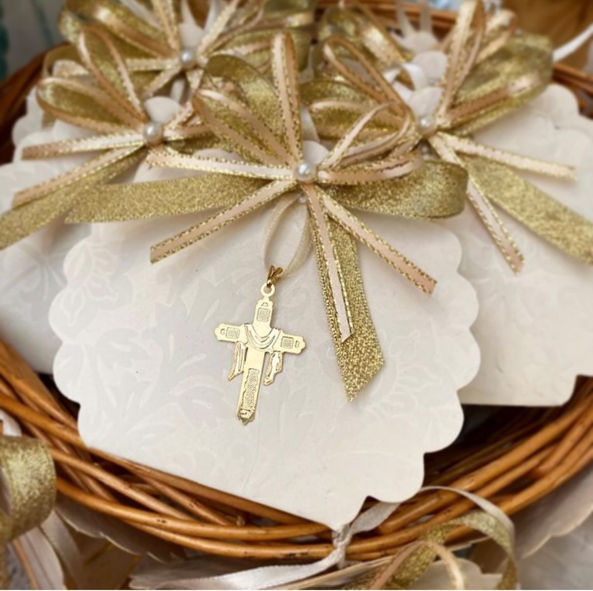 Una cesta llena de tarjetas blancas con cintas doradas y un colgante de cruz dorada.
