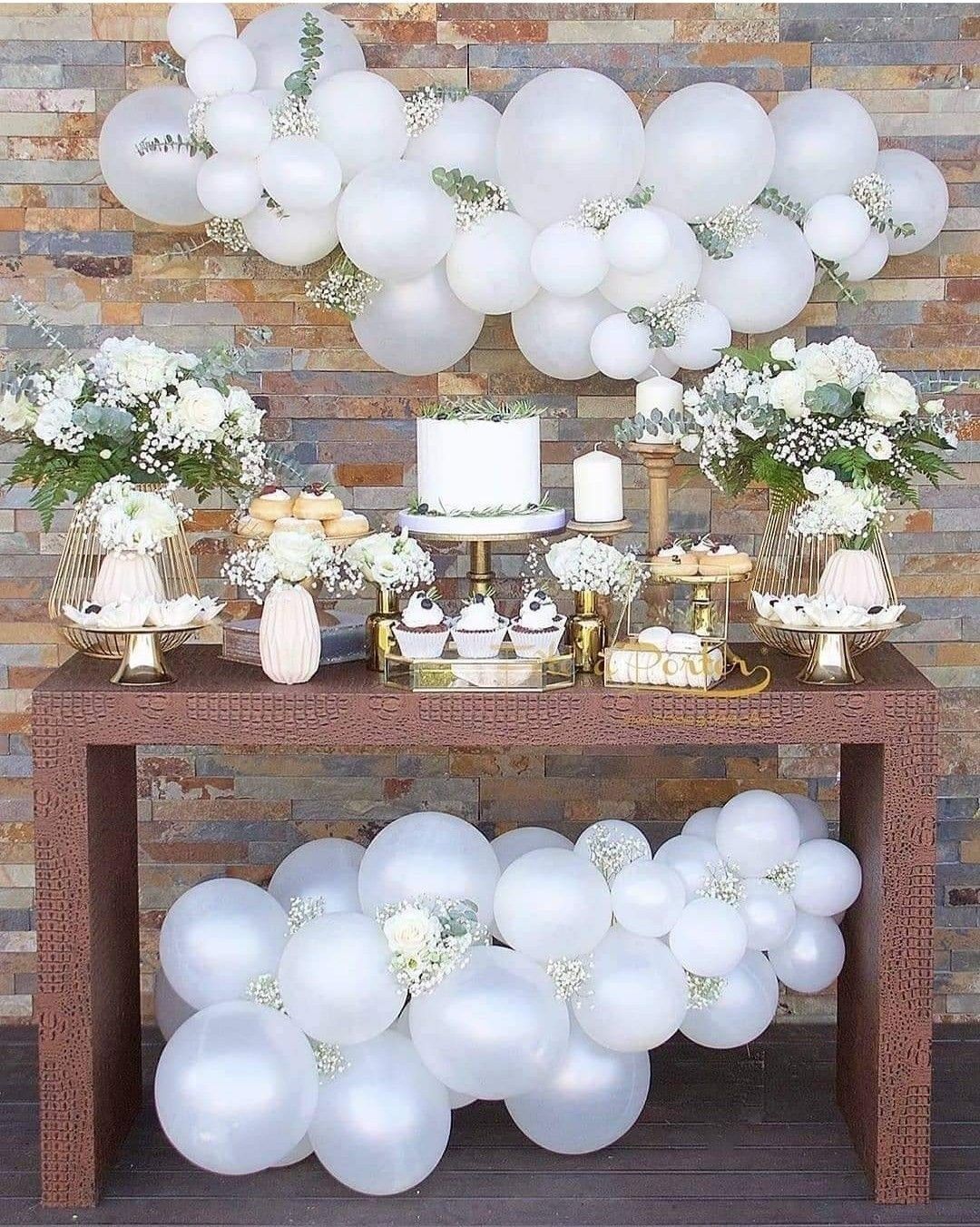 Una mesa decorada con globos blancos, flores y un pastel.