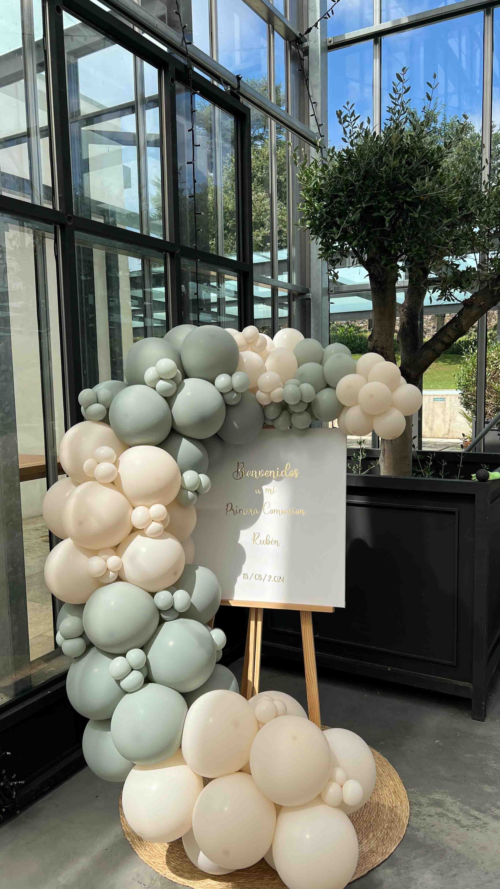 Un cartel con globos y flores está colocado encima de un caballete blanco.
