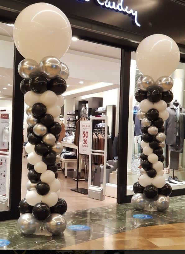 Dos columnas de globos blancos y negros frente a una tienda.