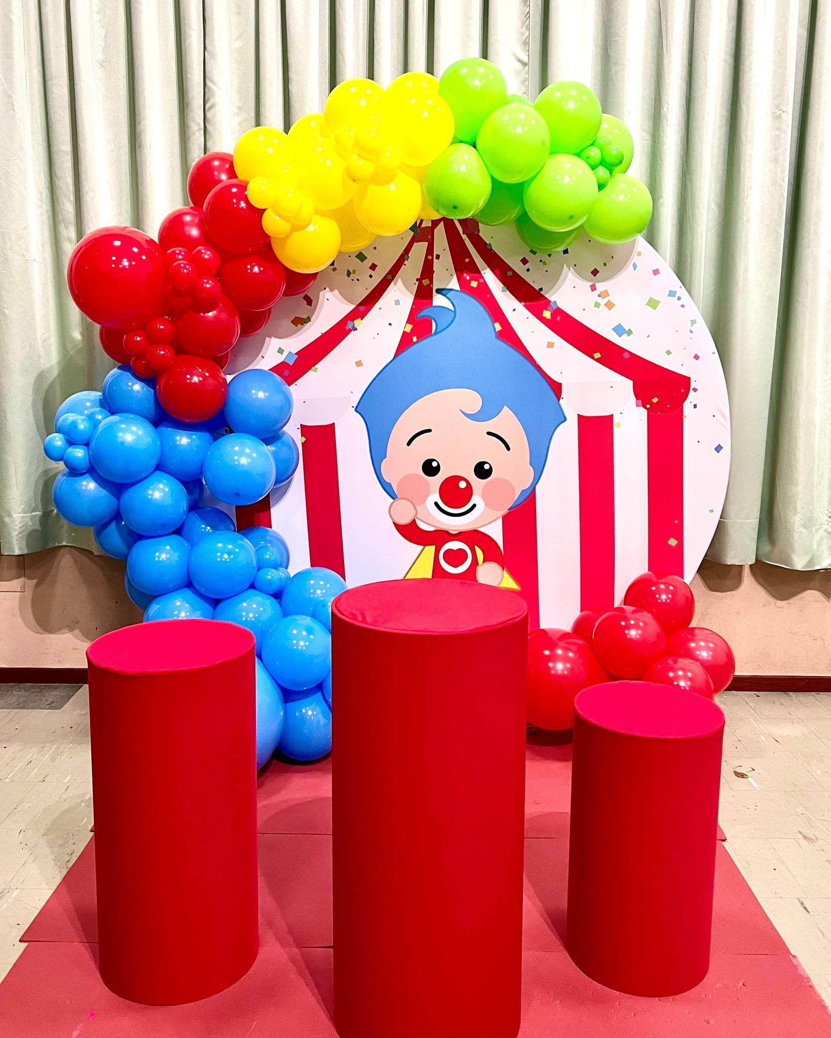 Un payaso está sentado frente a una carpa de circo rodeado de globos.