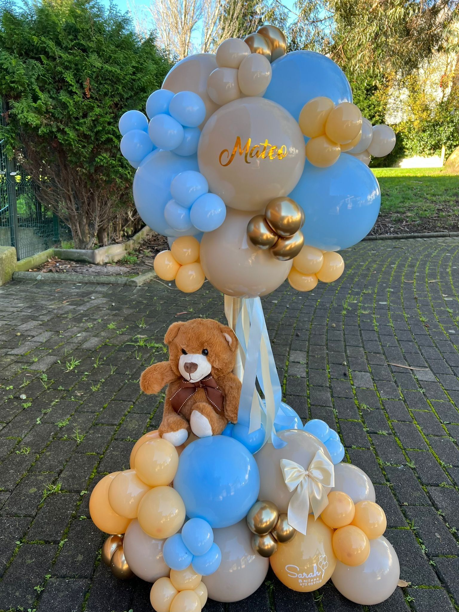 Un oso de peluche está sentado en la cima de un árbol hecho de globos.