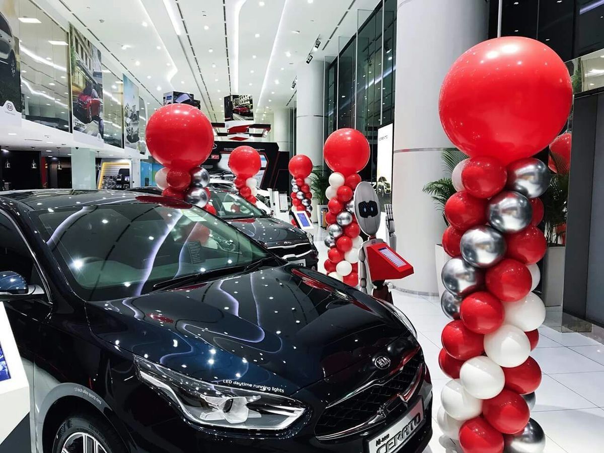 Un automóvil está estacionado en una sala de exposición decorada con globos rojos, blancos y plateados.
