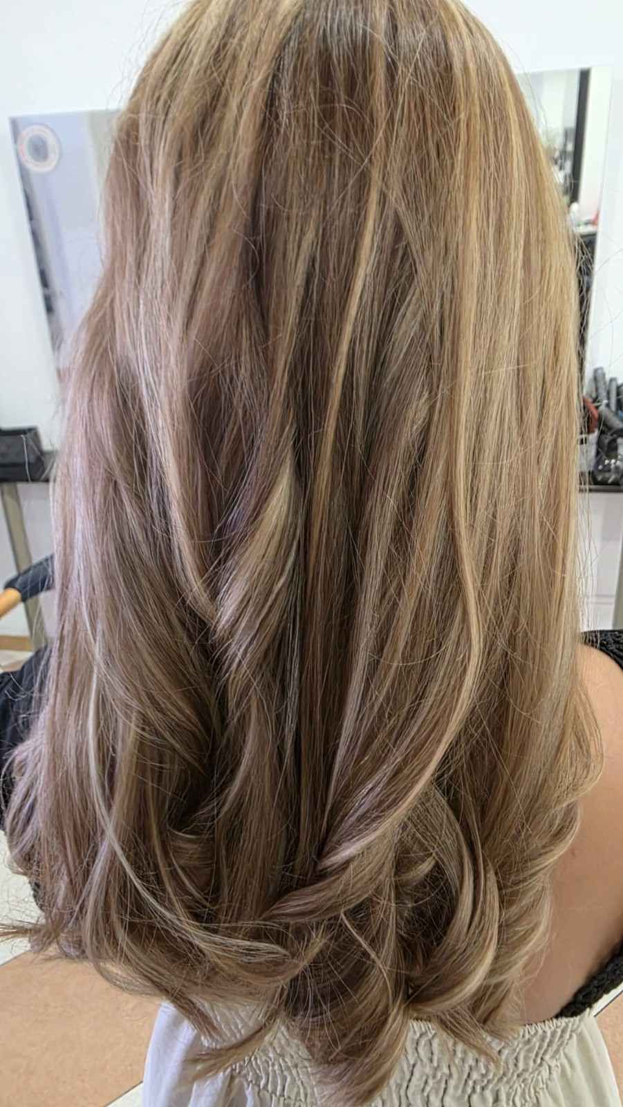 Cabello largo, rubio-castaño, con capas y peinado en suaves ondas, visto desde atrás.