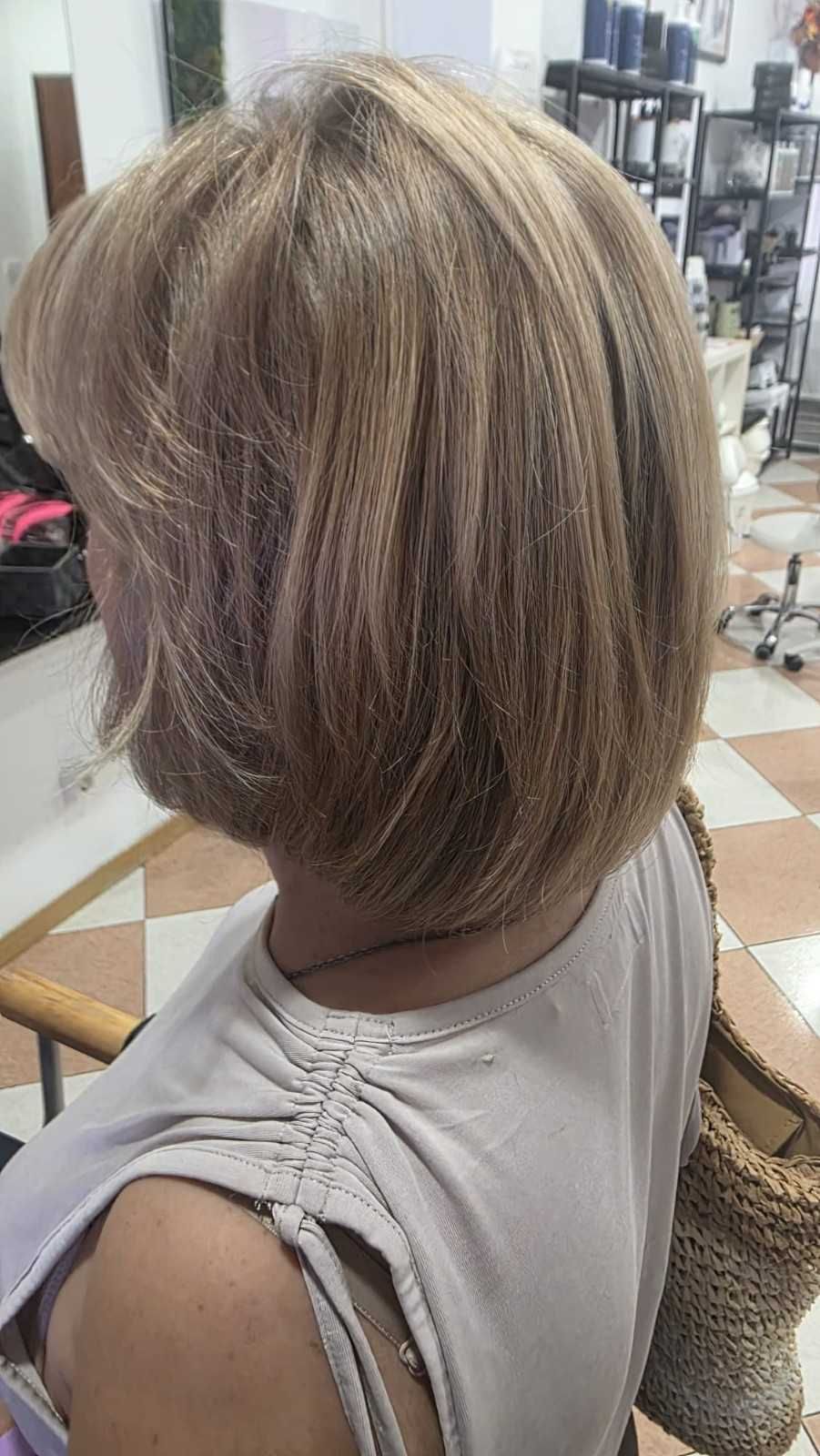 Vista lateral de un corte de pelo corto a capas rubio-castaño en una silla de peluquería, con un espejo y herramientas de peinado cerca.