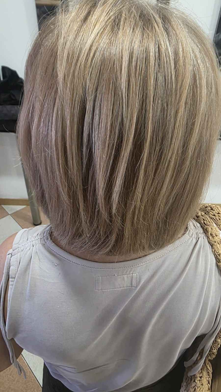Vista trasera de una persona con cabello rubio corto y capeado que lleva una blusa gris claro.