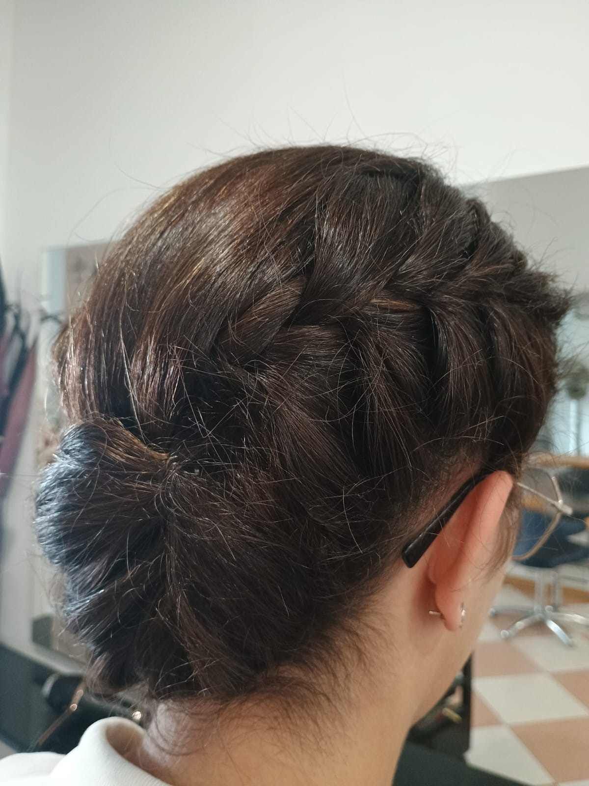 Parte posterior de la cabeza de una mujer con cabello oscuro recogido en un moño trenzado, sujeto con una pinza negra para el cabello.