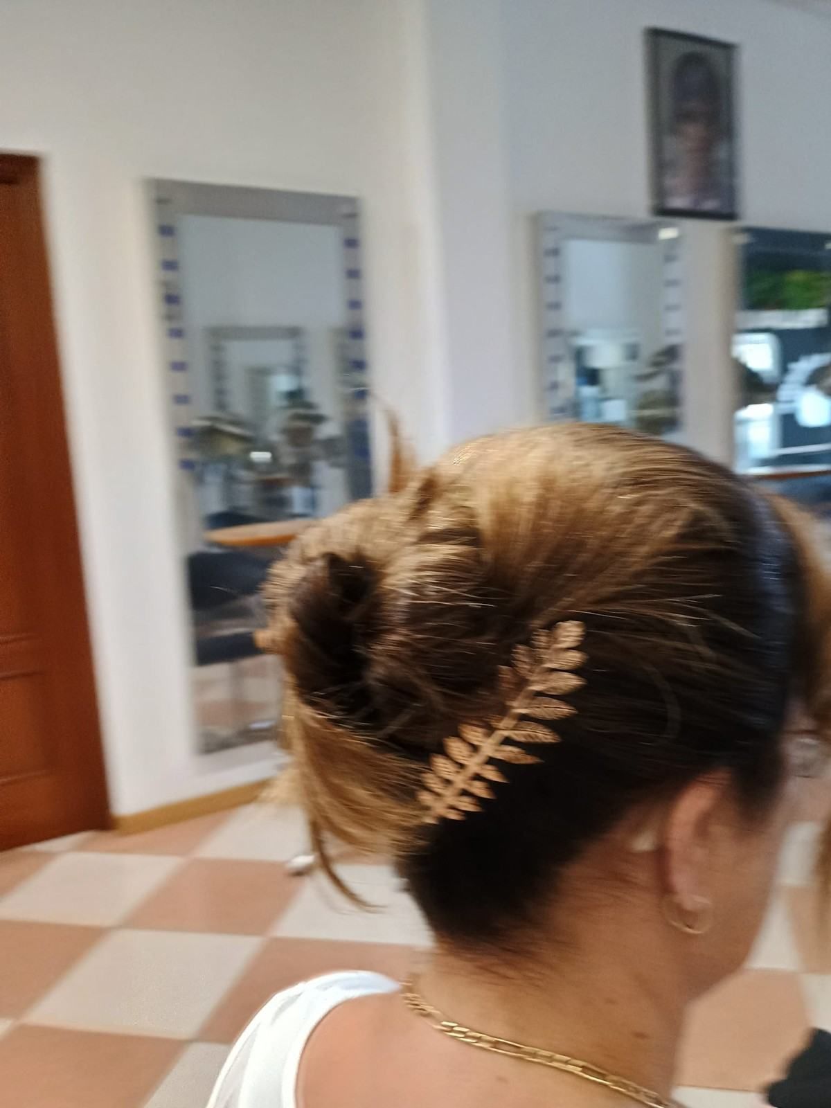 Moño con pinza dorada visto desde atrás en una habitación con espejos y suelo de baldosas a cuadros.