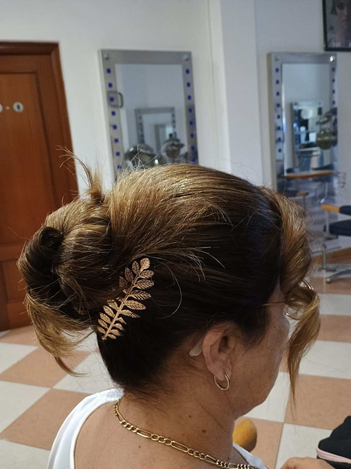 Mujer con un elegante moño trenzado y un accesorio dorado para el cabello, vista de perfil en interiores.