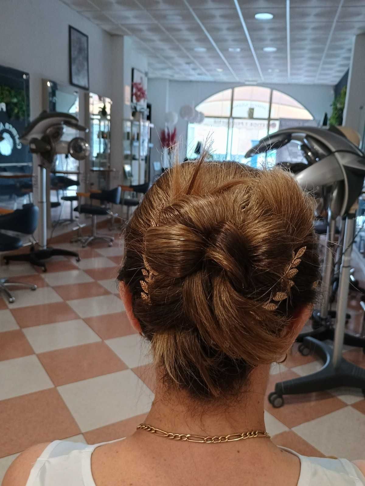 Persona con moño trenzado de pie en una peluquería, con sillones de peluquería y espejos al fondo.