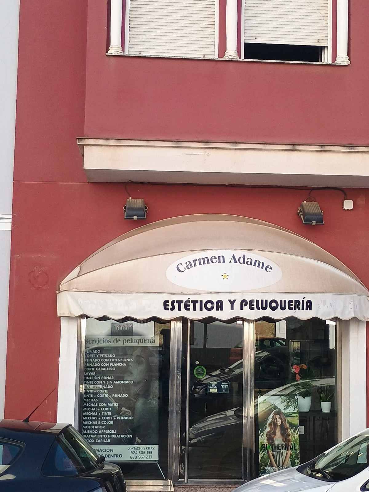 Local comercial con fachada roja y toldo que dice “ESTÉTICA Y PELUQUERÍA”, junto a un coche aparcado.