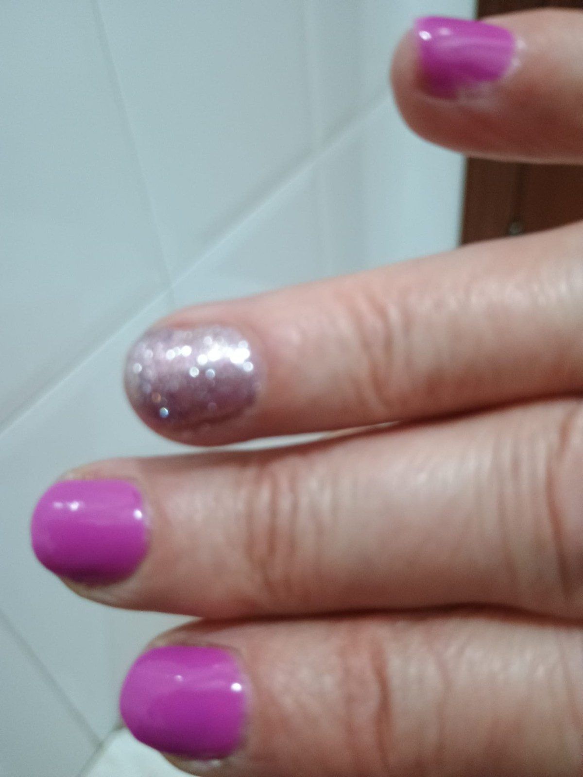 Mano con esmalte de uñas rosa y plateado brillante en tres uñas.