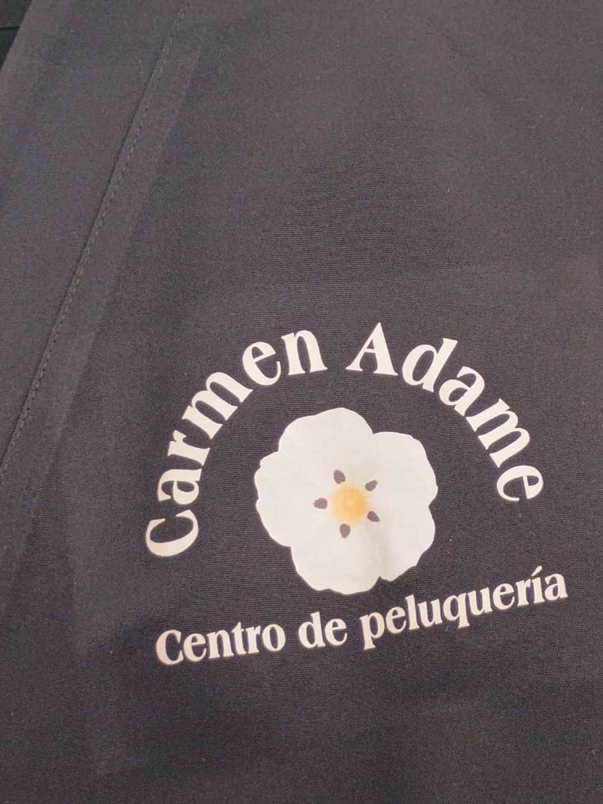 Letrero para Carmen Ada, Centro de peluquería, con un logotipo de una flor blanca sobre fondo oscuro.