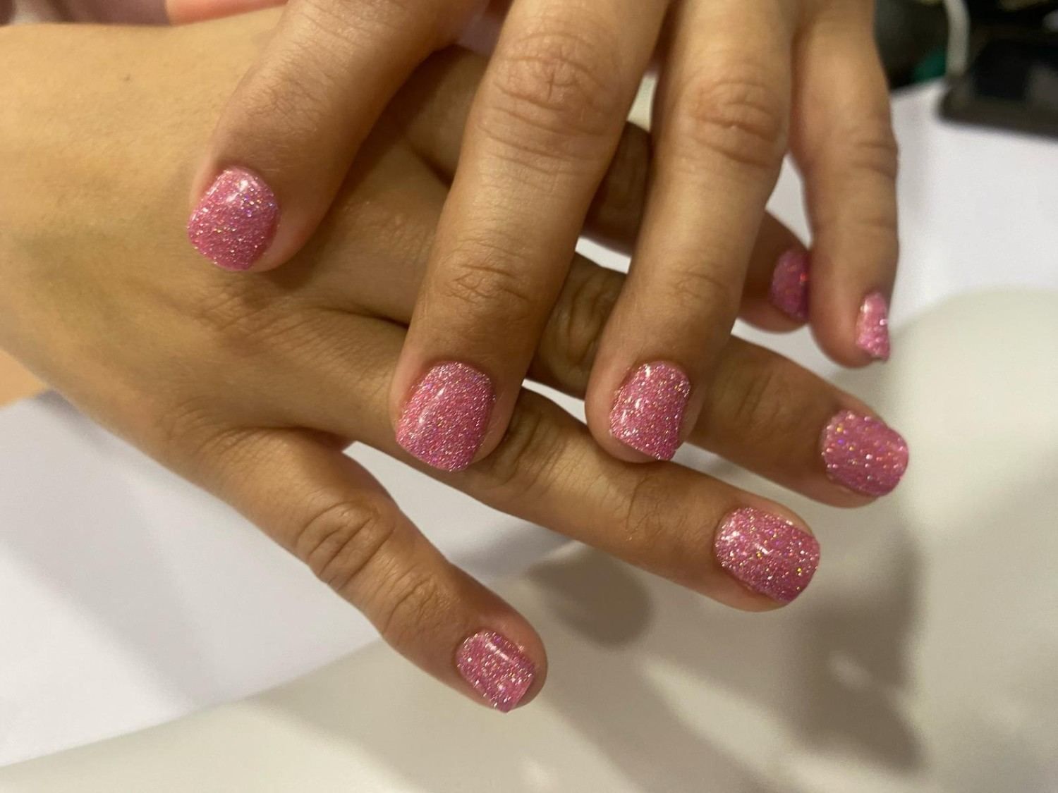 Manos con esmalte de uñas rosa brillante, apoyadas juntas sobre una superficie clara.