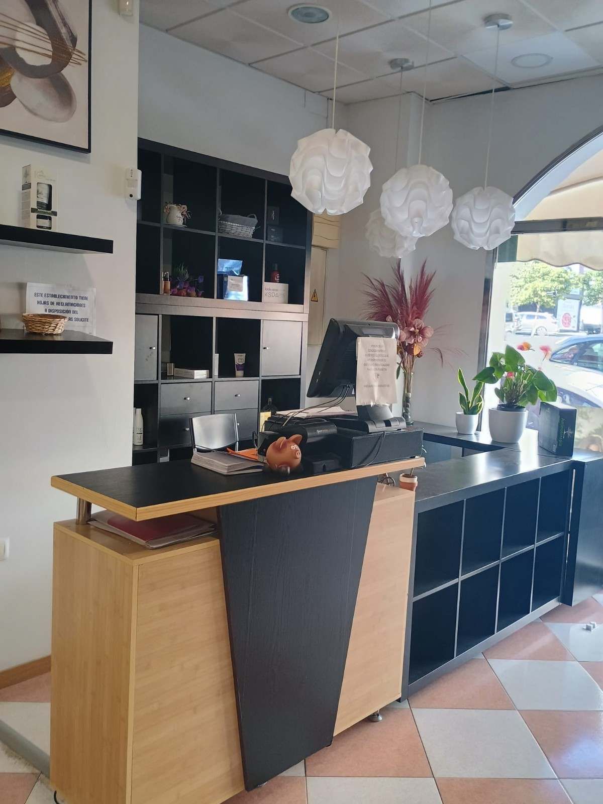 Barra de cafetería moderna con estantes negros, luces blancas colgantes y suelo de baldosas a cuadros.