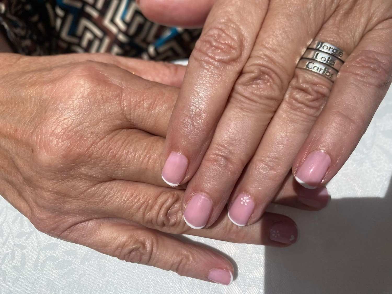 Manos con uñas pintadas de rosa, juntas, luciendo un anillo de plata.