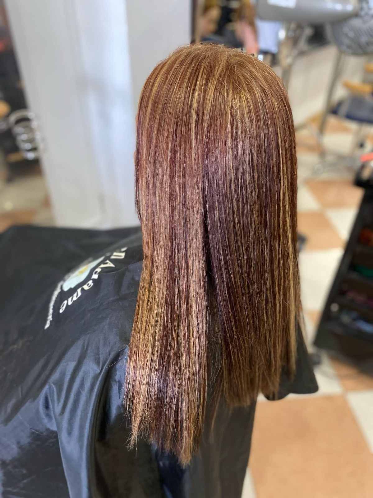 Cabello liso, castaño rojizo con sutiles reflejos en una silla de peluquería.