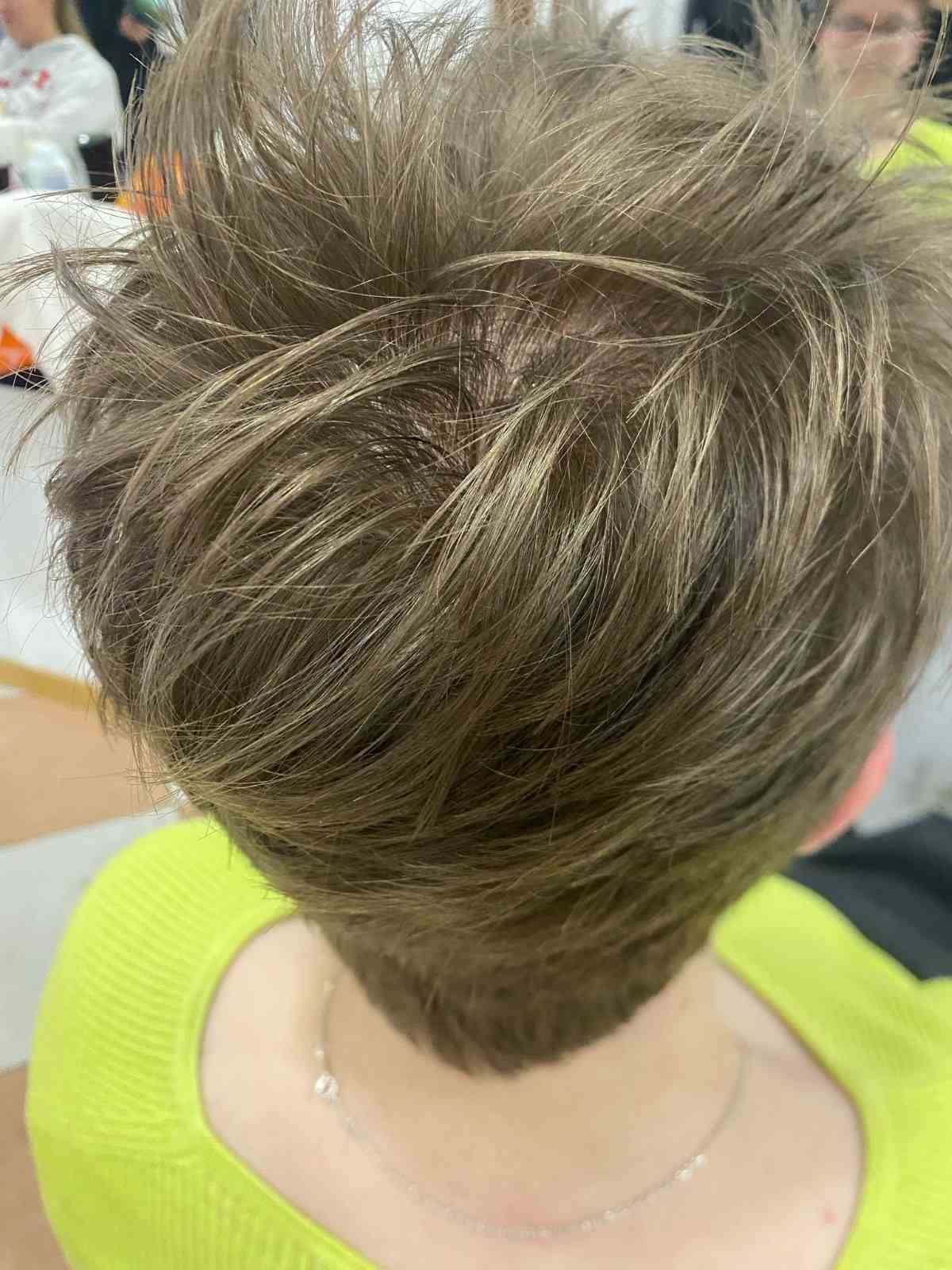 Corte de pelo corto y puntiagudo de color castaño con reflejos rubios visto desde atrás, combinado con una blusa de color amarillo neón.