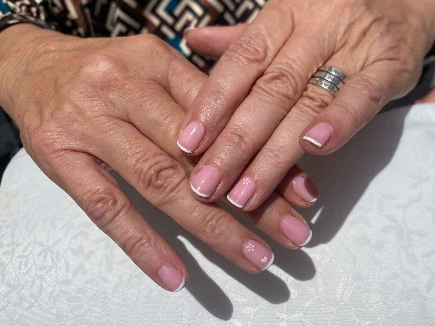 Manos con uñas pintadas de rosa descansando sobre una superficie blanca, una de ellas con un anillo de plata.