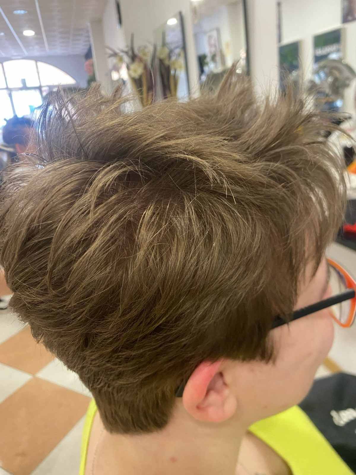 Corte de pelo castaño desaliñado con rapado lateral, visto de perfil en una silla de peluquería.