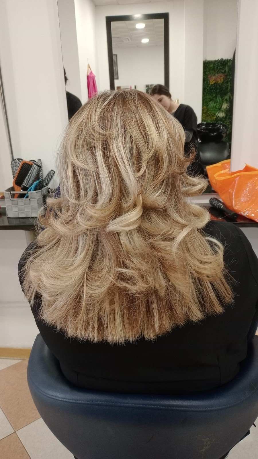 Cabello rubio, ondulado y a la altura de los hombros, con capas con mechas, visto desde atrás en una silla de peluquería.