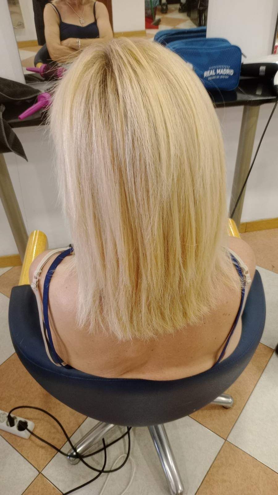 Corte de pelo bob rubio visto desde atrás en una silla de peluquería con herramientas para el cabello en el suelo cerca.