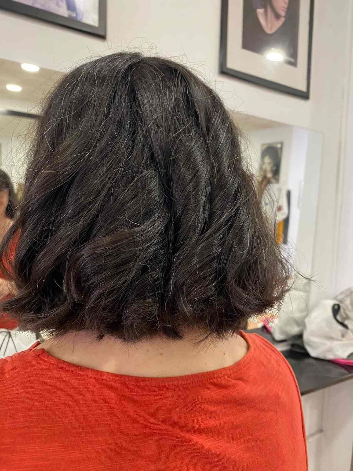 Vista trasera de una persona con cabello corto y oscuro, vestida con una blusa roja, sentada en una peluquería.