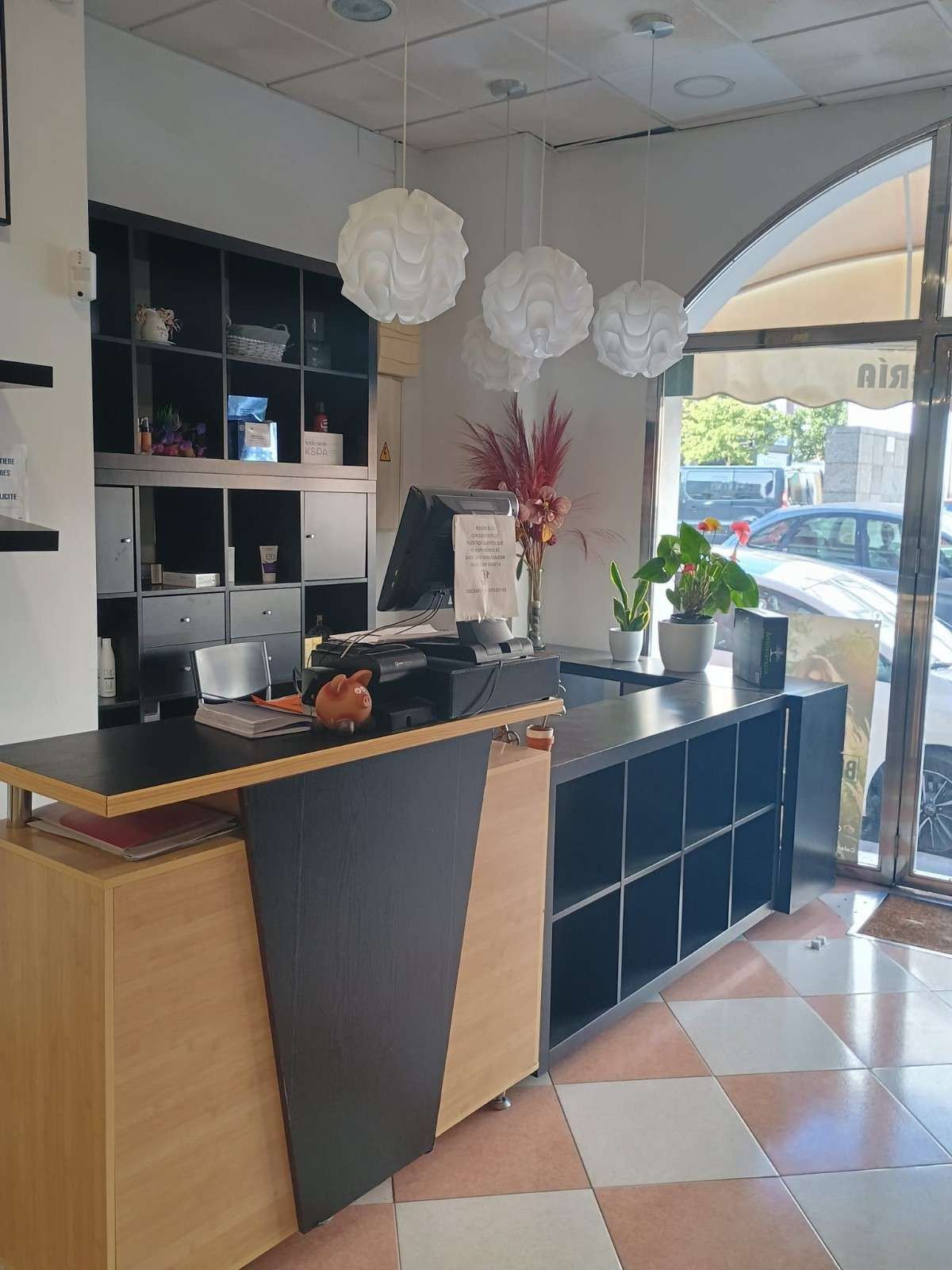 Interior de cafetería moderna con mostrador de madera y negro, lámparas colgantes y ventana arqueada.