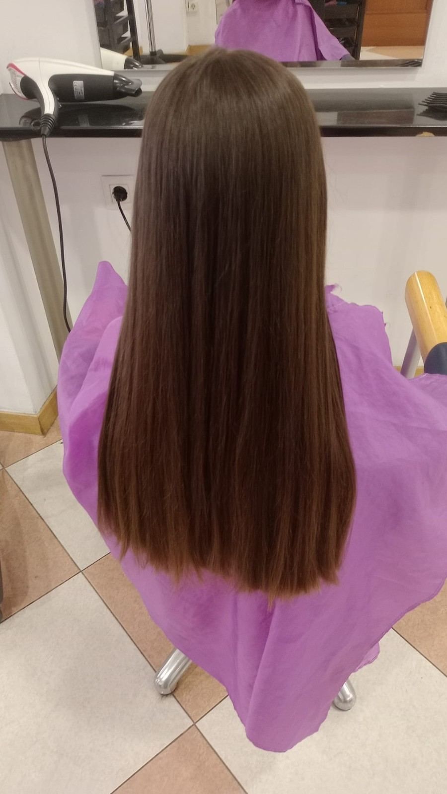 Cabello largo, liso y castaño, cubriendo una capa morada de peluquería en una silla de salón.