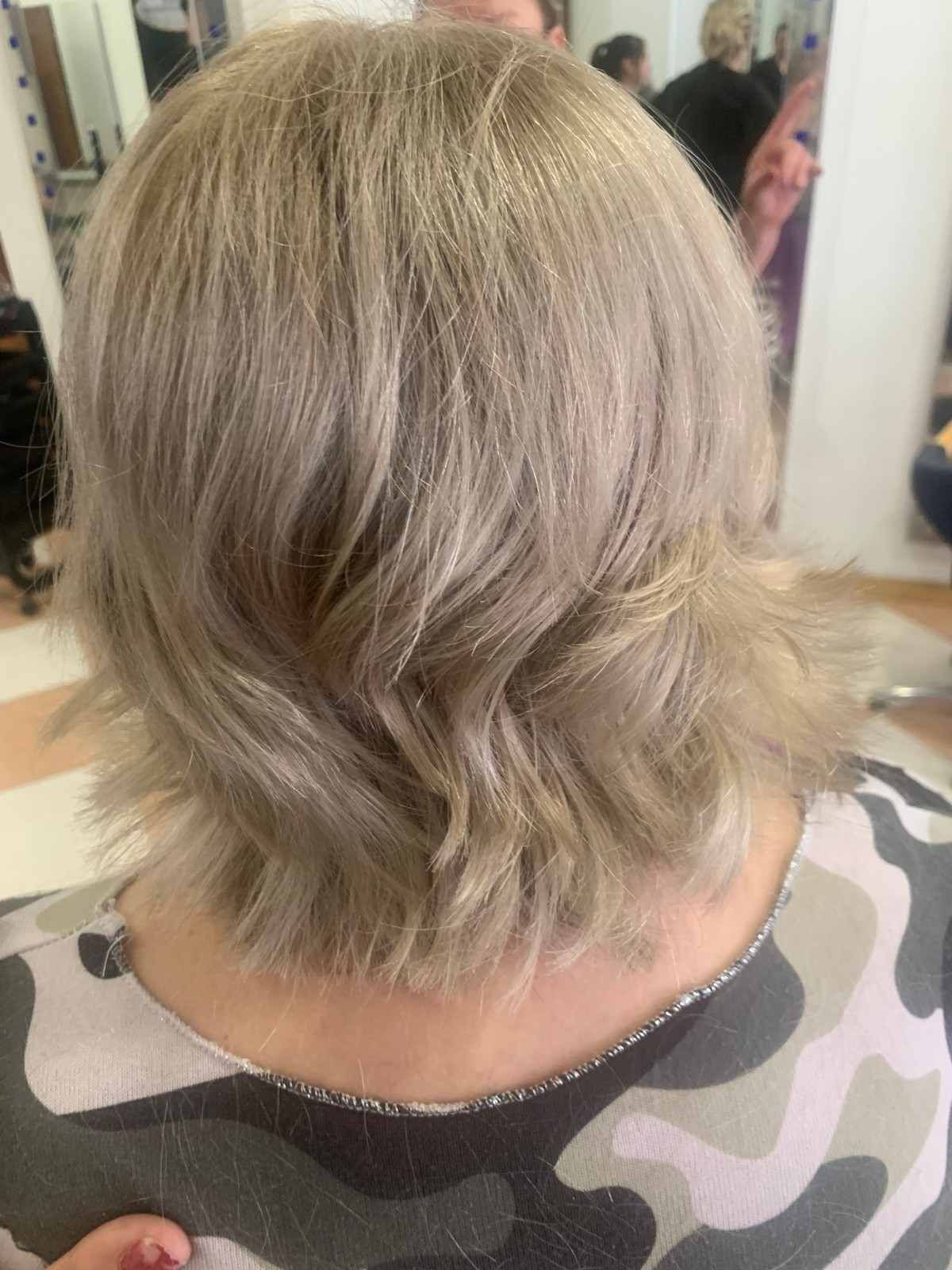 Corte de pelo corto, rubio plateado, con capas y suaves ondas, visto desde atrás.