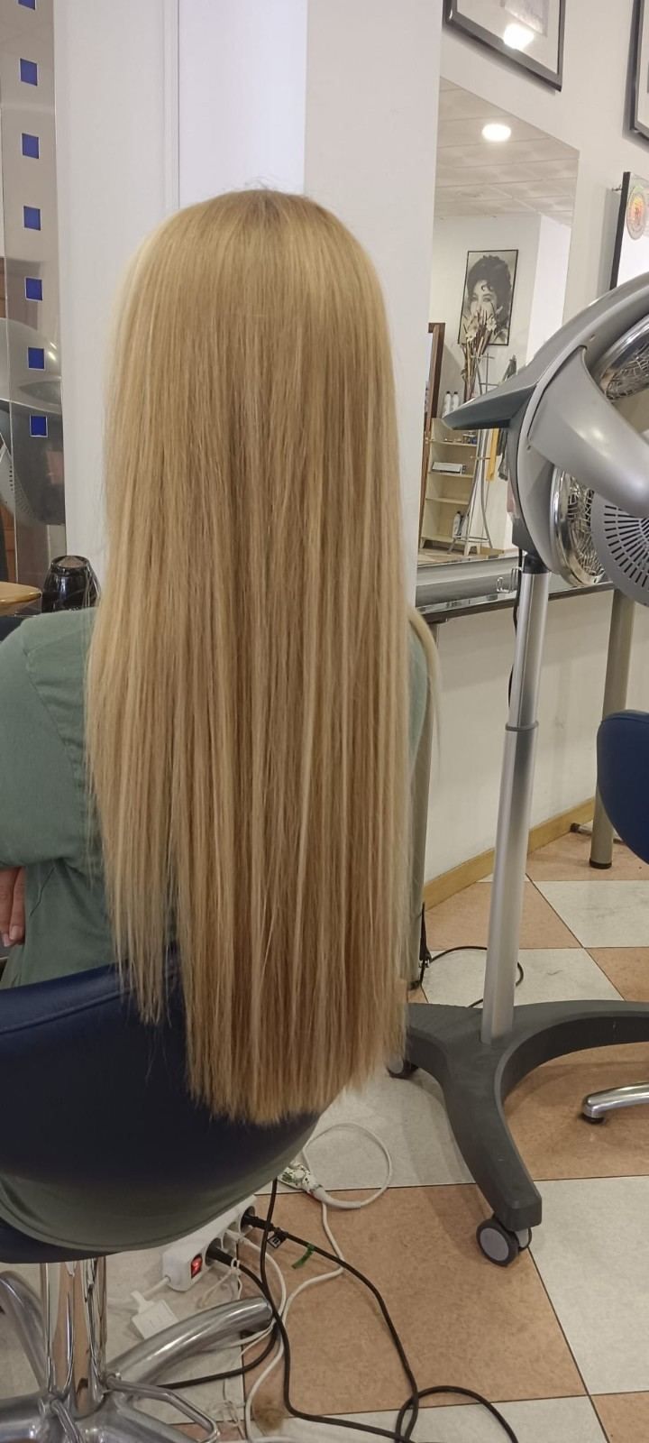 Una persona sentada en una peluquería luce una larga melena rubia y lisa, con herramientas de peinado a su alcance.