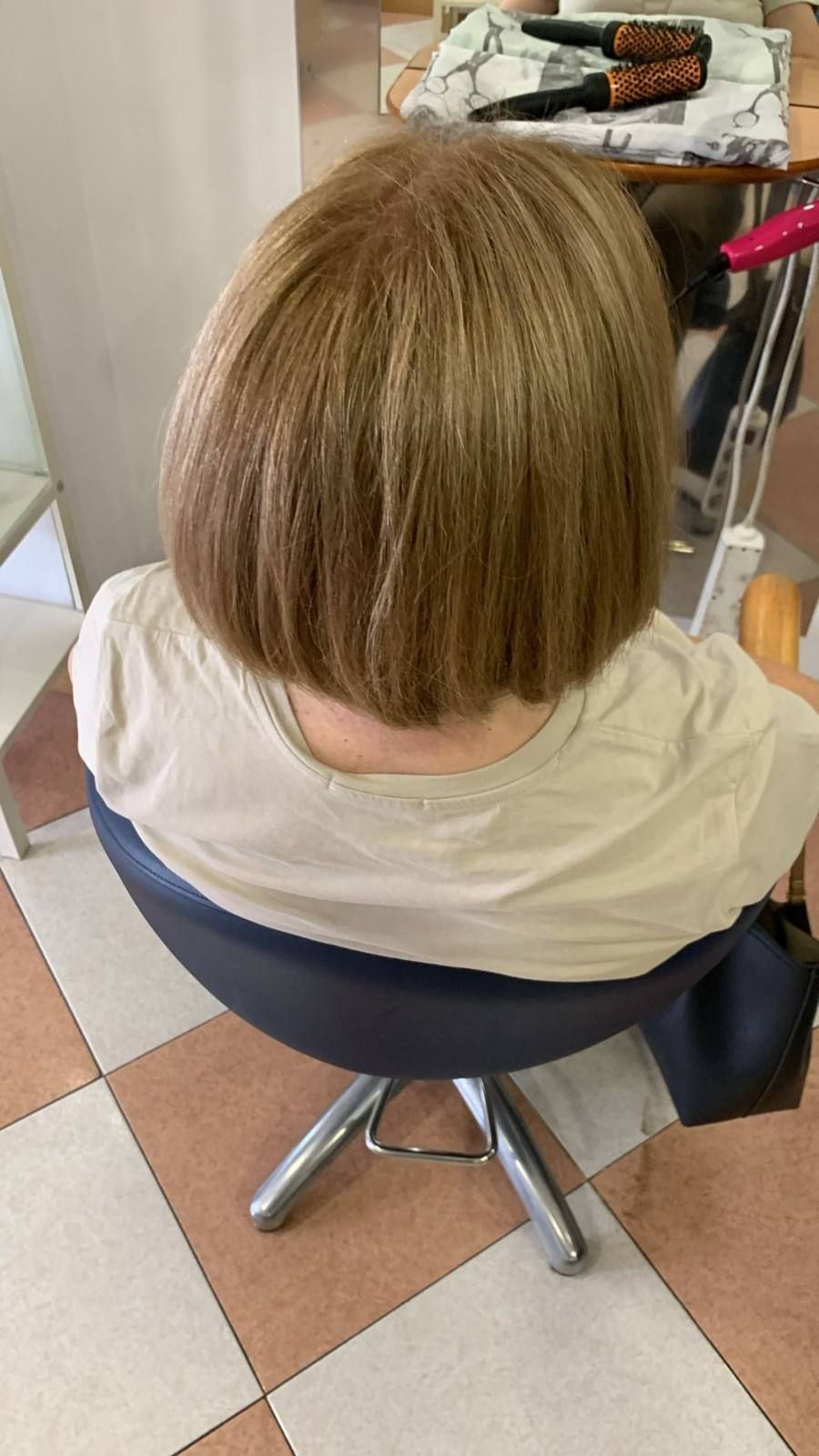 Persona con cabello corto castaño claro sentada en una silla de peluquería, vista desde atrás.