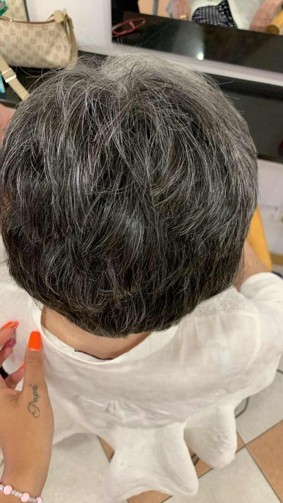 Vista superior de una persona con cabello corto entrecano, con una mano sosteniendo un frasco rociador cerca de la cabeza.