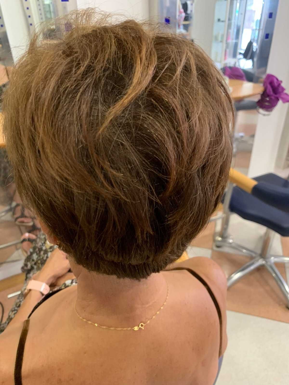 Corte de pelo corto castaño a capas, visto desde atrás en una silla de peluquería.