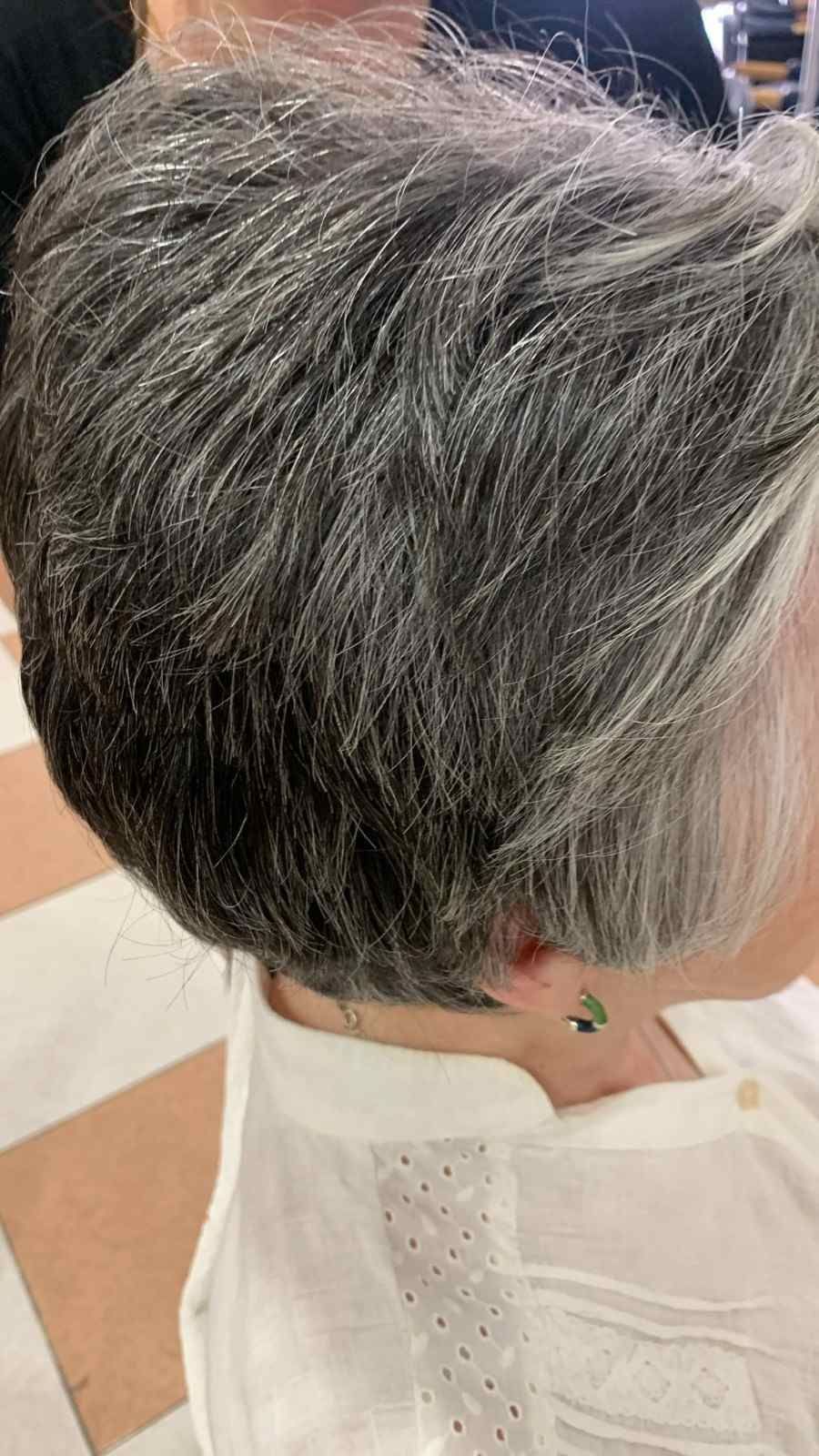 Corte de pelo pixie corto y gris visto de perfil, con una capa blanca estampada en una peluquería.