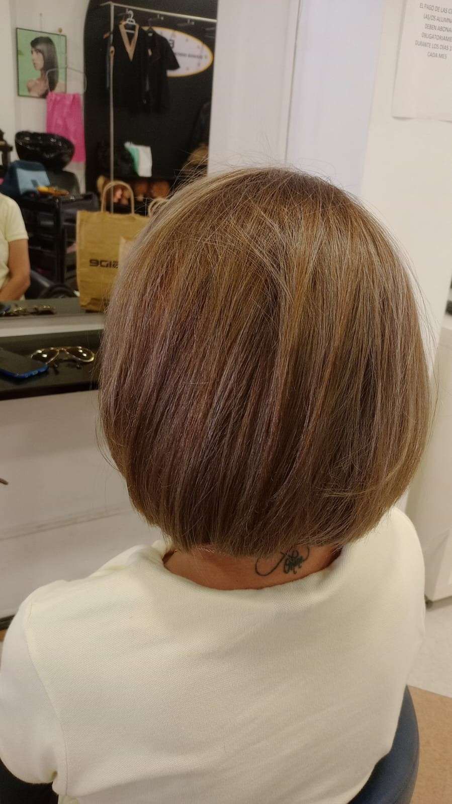 Parte posterior de la cabeza de una persona mostrando un corte de pelo corto y castaño en capas en el espejo de una peluquería.